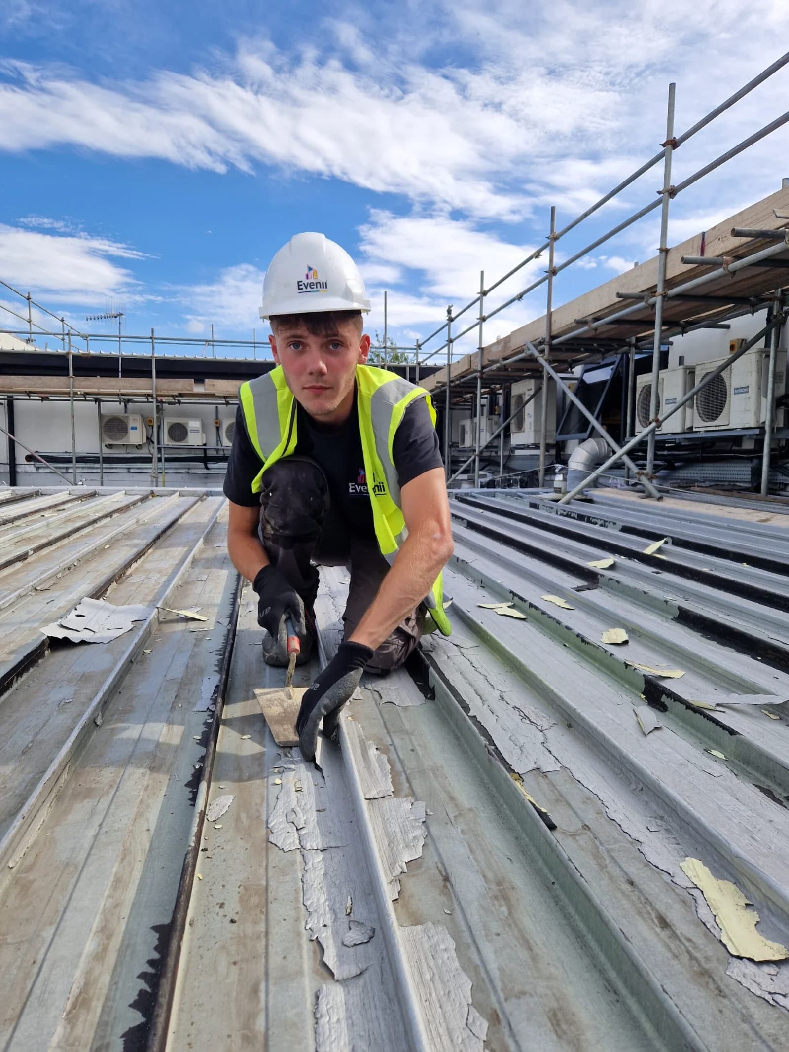 Roofer in branded hi-vis and harness working on a commercial metal roof in the North East